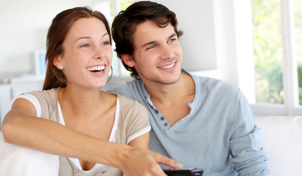 Attractive couple watching television in their flat, London City Mortgages