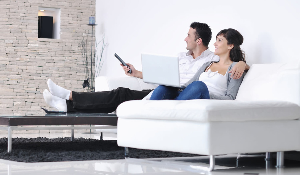 Couple watching TV while accessing their laptop news, London City Mortgages