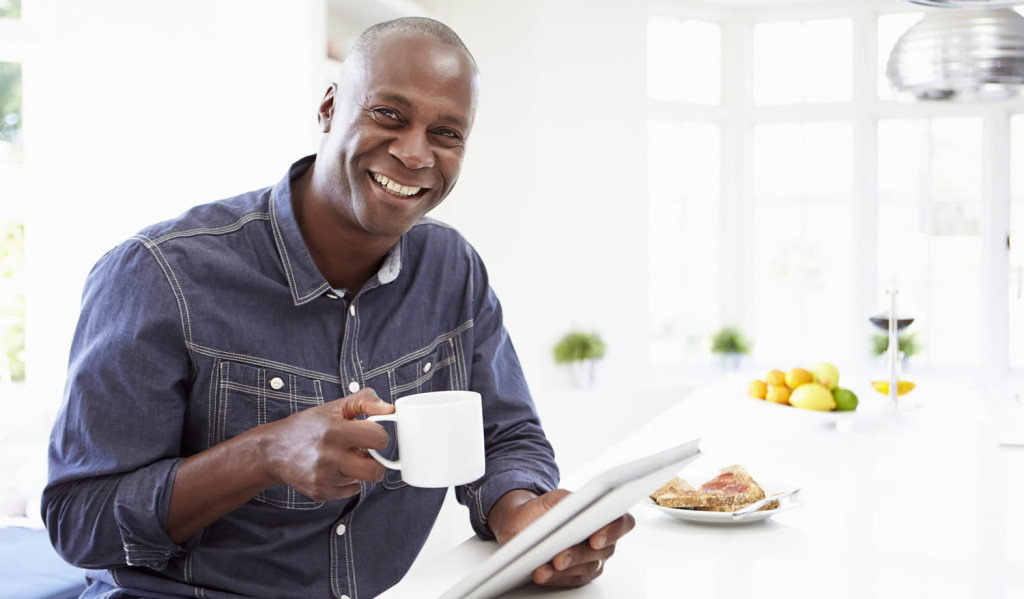 Happy man having breakfast receiving notices on his tablet, London City Mortgages