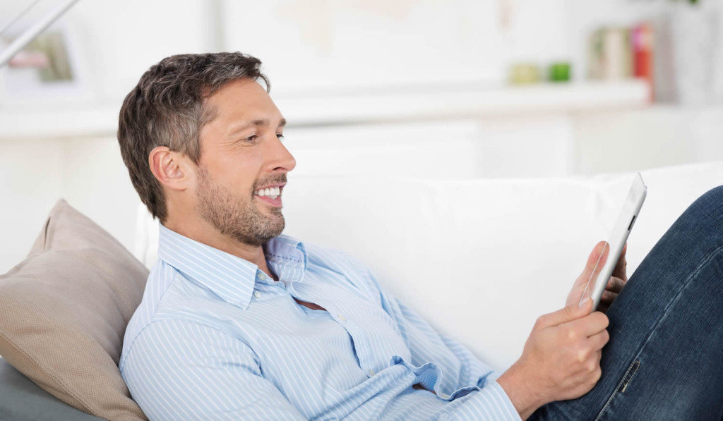 Mature man relaxing on the sofa reviewing his tablet news, London City Mortgages