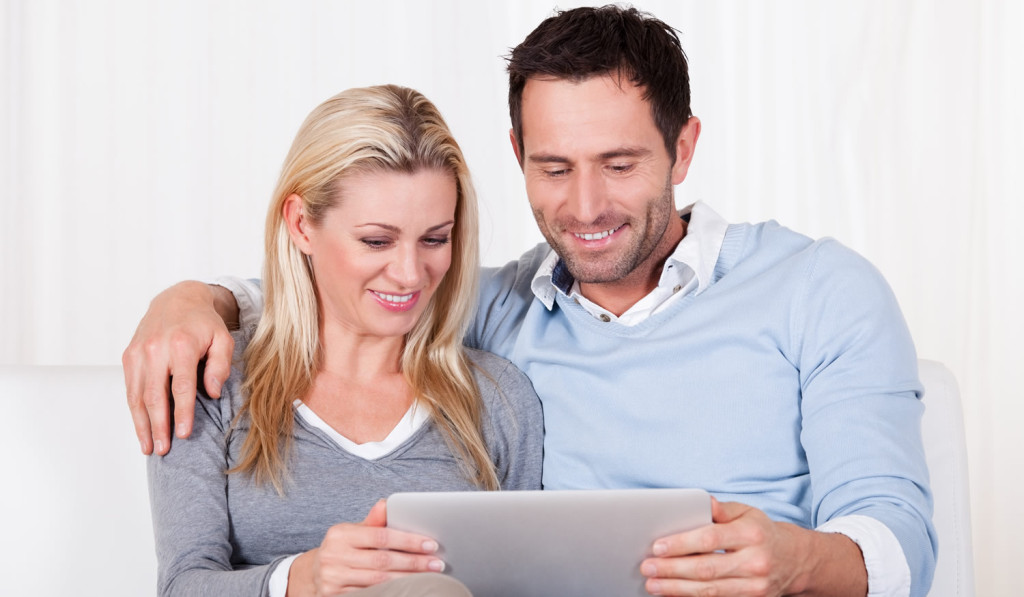 Livingroom smiling couple reviewing tablet updates London City Mortgages